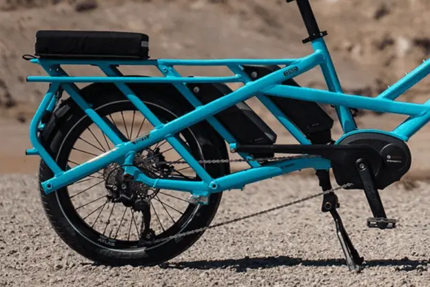 Side view of the seat and rear wheel of an electric bike. The bike is light blue. and has two batteries.