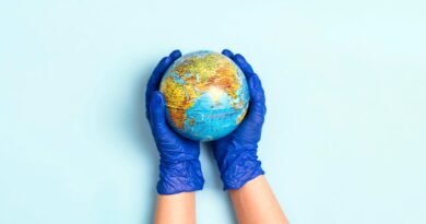 Two hands wearing blue disposable medical gloves cradle a globe, with Africa, Europe, and Asia visible.