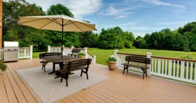 A large wooden backyard deck with a white railing and a square table with wooden benches next to green grass.