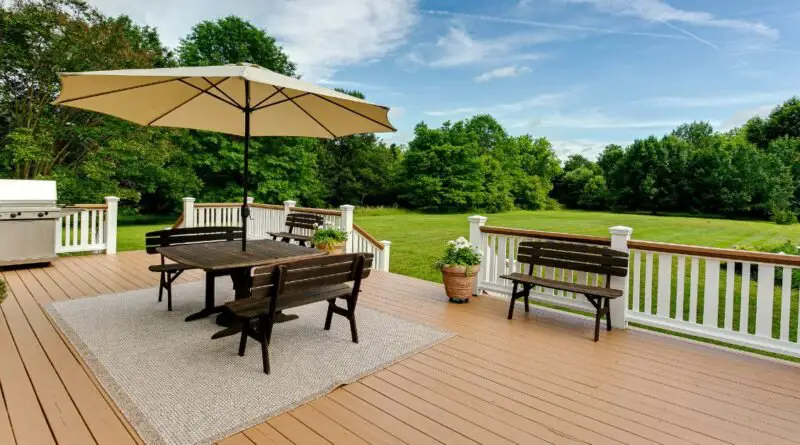 A large wooden backyard deck with a white railing and a square table with wooden benches next to green grass.