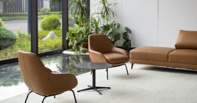 A brown leather sofa and two chairs inside a room with concrete floors, a small pond with plants, and large windows.