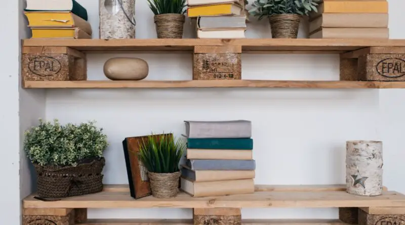 A set of two shelf bookcases against a white wall holding books and plants made out of old wooden pallets.