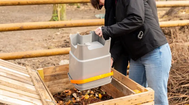 A gardener and nature enthusiast outside at their garden boxes, mixing their homemade compost in jeans and a jacket.
