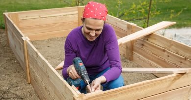 A smiling person is using an electric screwdriver to screw a screw into the wood. They're building something.
