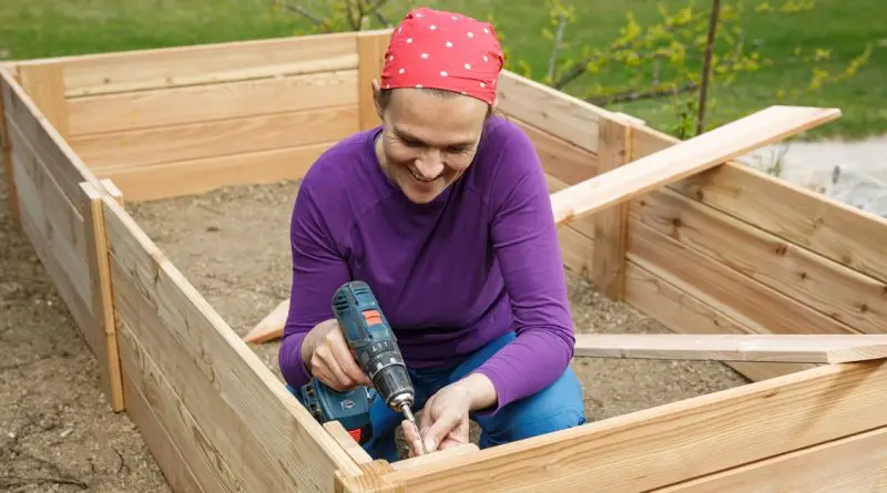 A smiling person is using an electric screwdriver to screw a screw into the wood. They're building something.