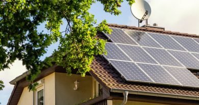 A two-story home with multiple rows of solar panels next to a large dish antenna, and a tree at the front of the house.