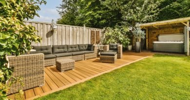 A backyard with a wooden fence, woven outdoor furniture with grey cushions, and a hot tub under a small pergola.
